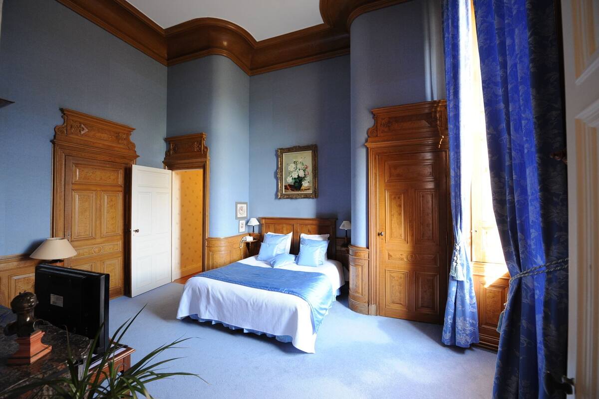 A bedroom with a large bed, wooden wardrobe, and a nightstand with a lamp.