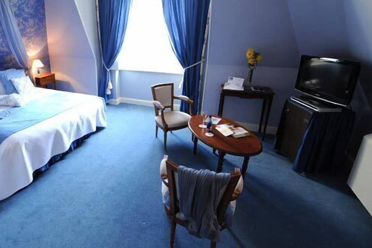 A bedroom with a bed, bedside tables, a chair, a table, a TV, and curtains.