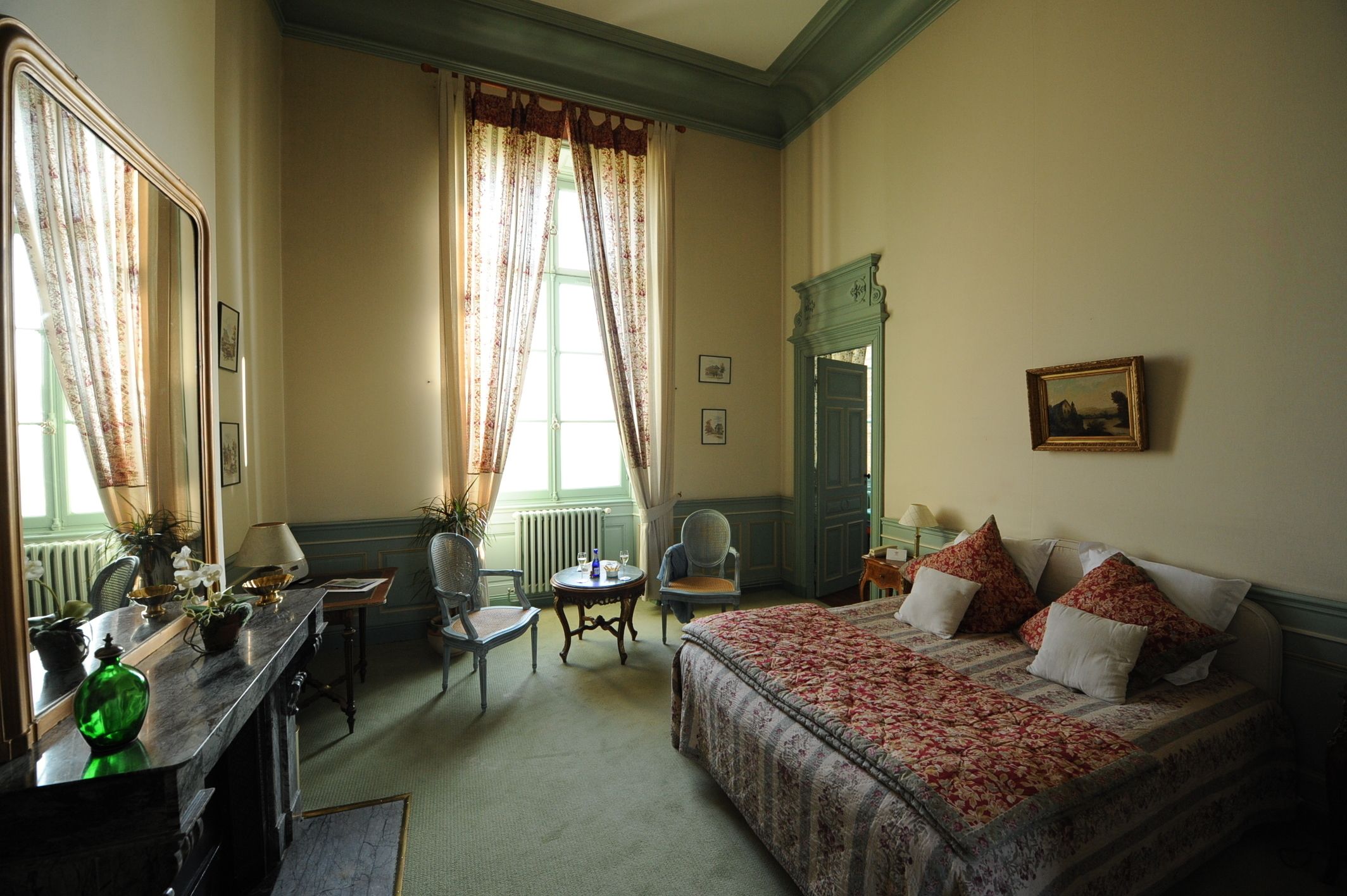 A bedroom with a bed, a desk, a chair, a window with curtains, and a painting on the wall.