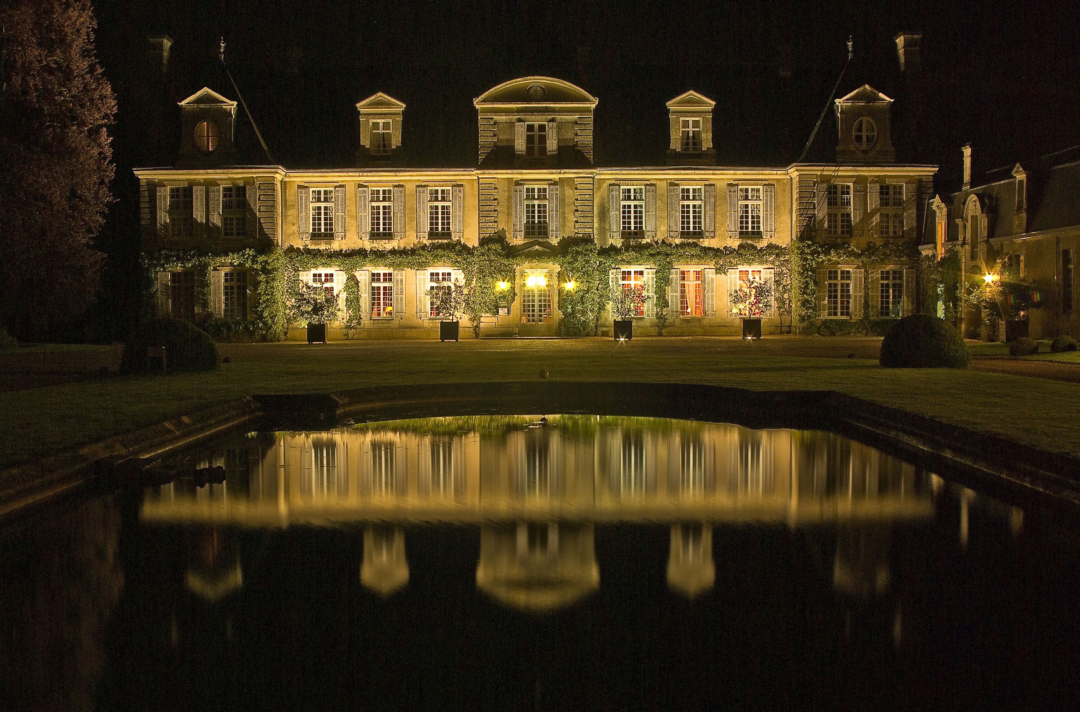 A large, illuminated building with a symmetrical facade, a central courtyard, and a reflecting pool.