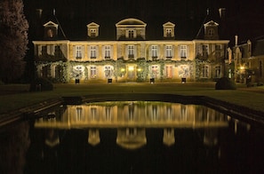 Un grand bâtiment illuminé, doté d’une façade symétrique, d’une cour centrale et d’un bassin décoratif.
