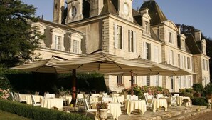 A historic building with a large covered outdoor dining area, featuring multiple tables and chairs. - Château de Curzay (Curzay-sur-Vonne)