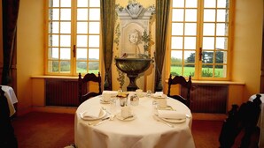 A dining room with a table set for four, large windows, and a decorative mantelpiece. - Château de Curzay (Curzay-sur-Vonne)