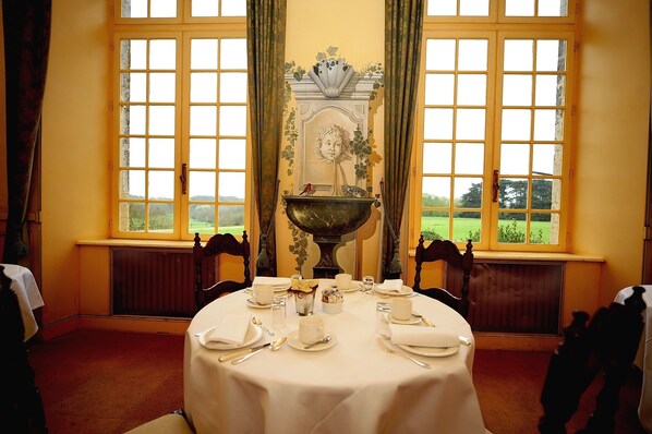 A dining room with a table set for four, large windows, and a decorative mantelpiece. - Château de Curzay (Curzay-sur-Vonne)