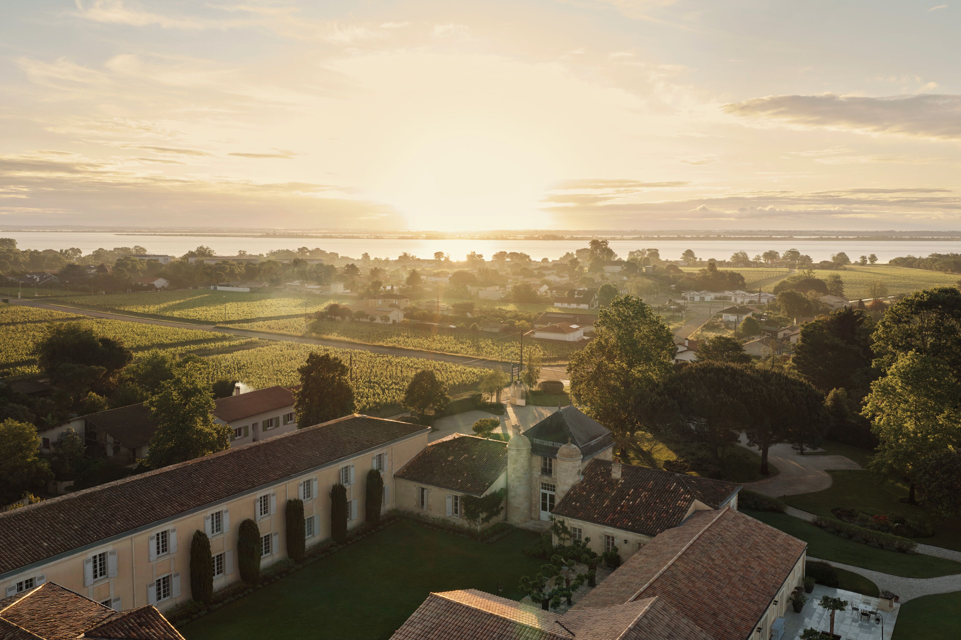 A large estate with multiple buildings, expansive green fields, and a body of water in the background.