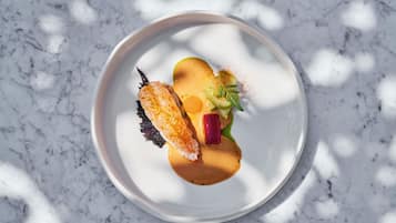A white plate with a fish, a beet, and a green garnish on a marble surface.