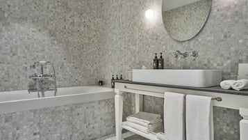 A bathroom with a marble mosaic wall, a white bathtub, a sink with a mirror above, and two towels on the counter.