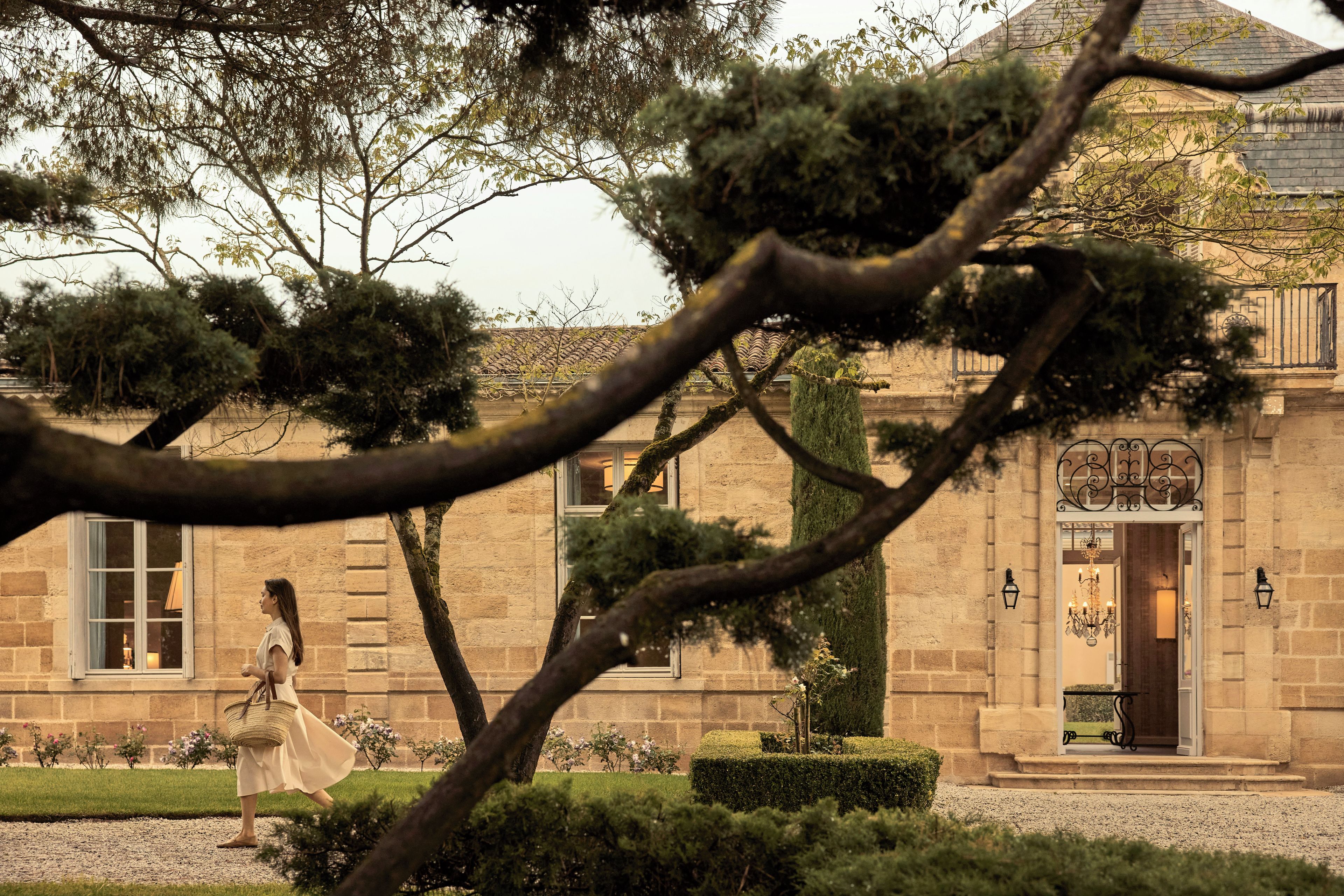 A woman walking in a garden with a building in the background.