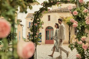 Una pareja caminando por una calle adoquinada con un arco floral, edificios históricos y un cielo despejado.