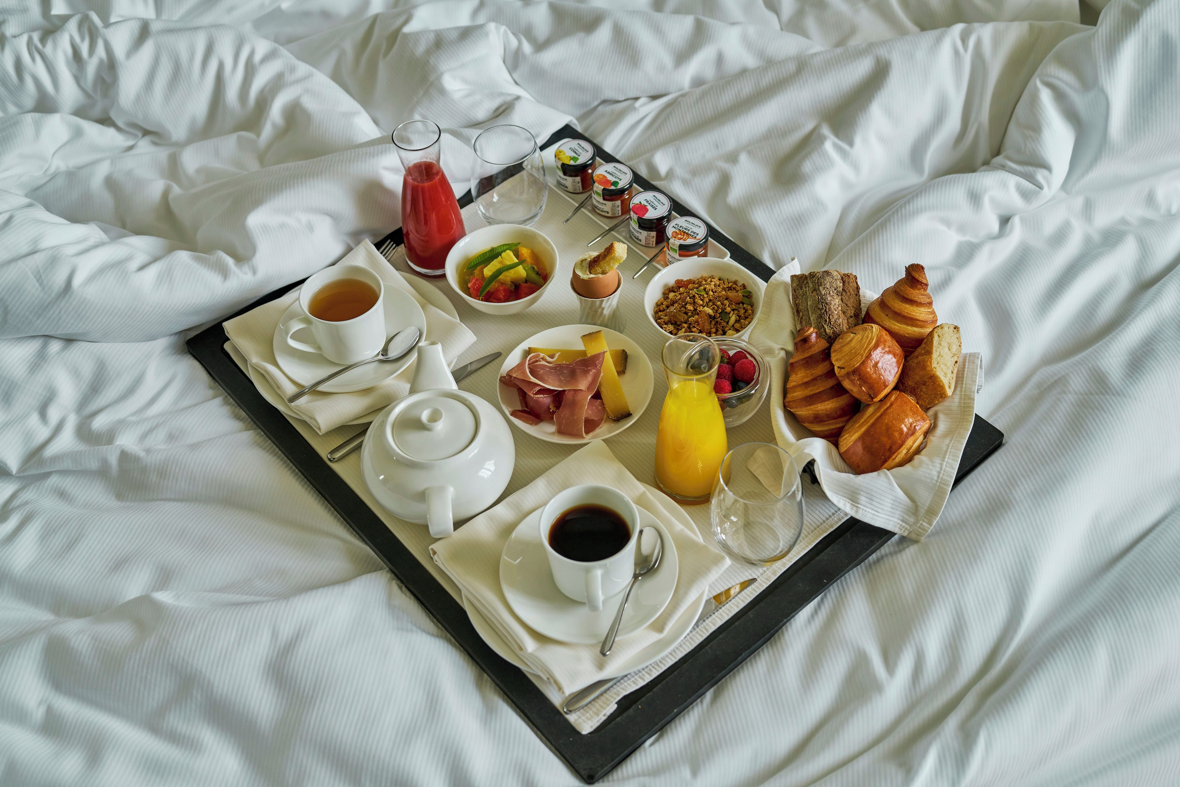 Bandeja de desayuno con diferentes alimentos y bebidas sobre una cama.