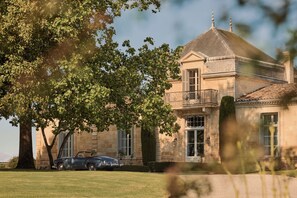 A large stone building with a prominent tower, a balcony, and a classic car parked in front. - COMO Cordeillan‑Bages (Pauillac)