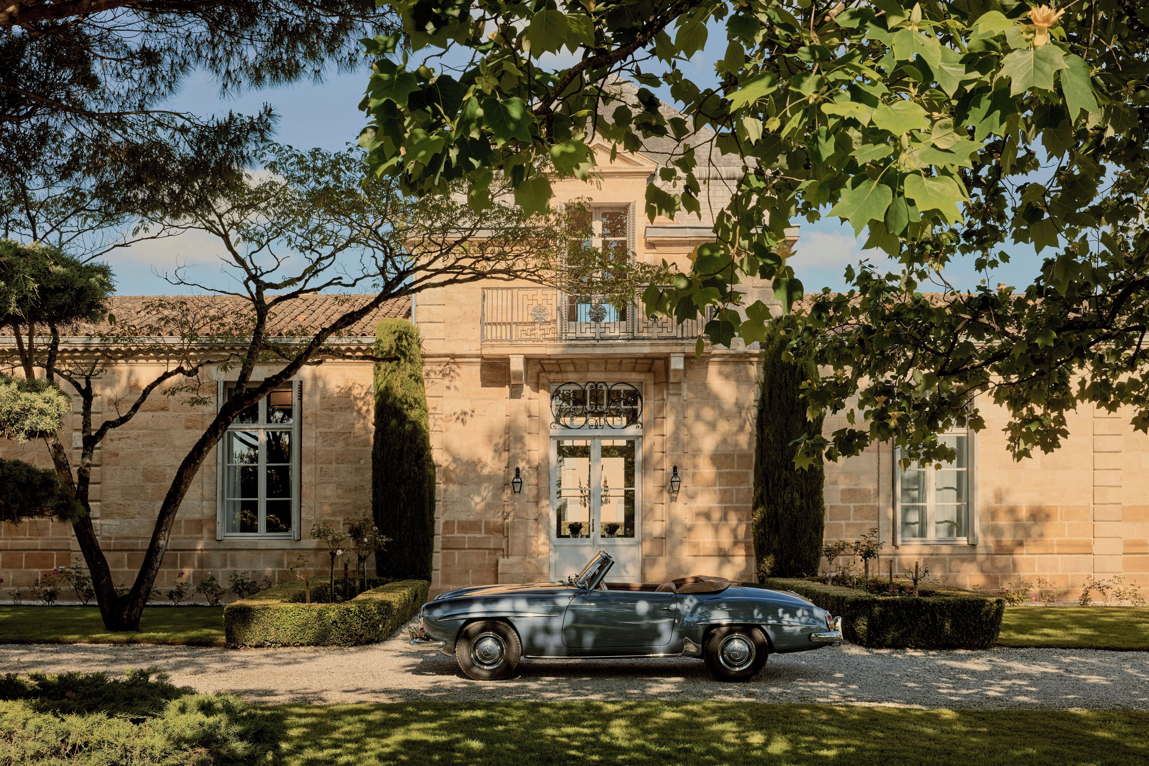 A classic convertible car parked in front of a historic building with a balcony and large windows.