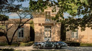 A classic convertible car parked in front of a historic building with a balcony and large windows.