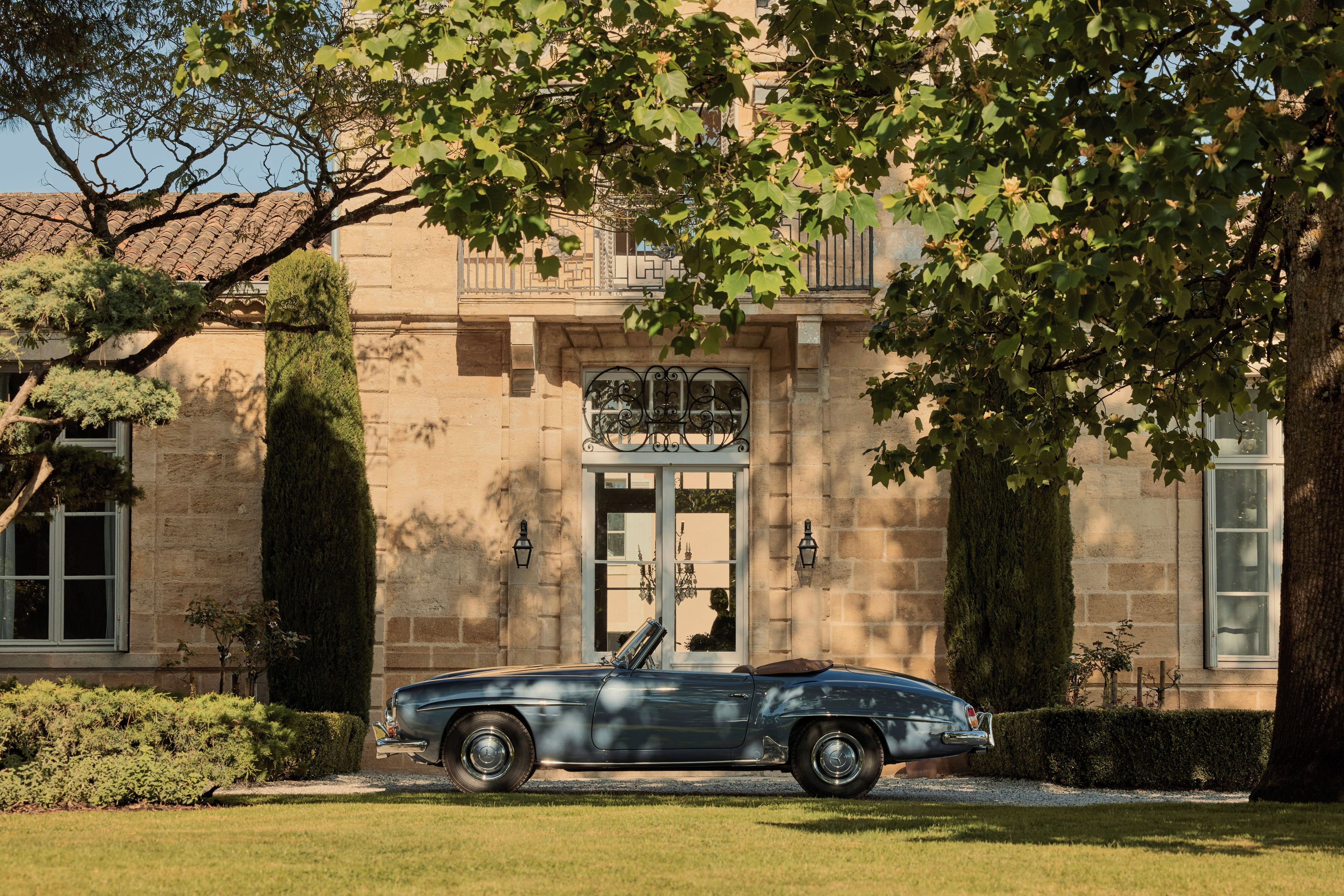 A vintage car parked in front of a stone building with a large window and a door.