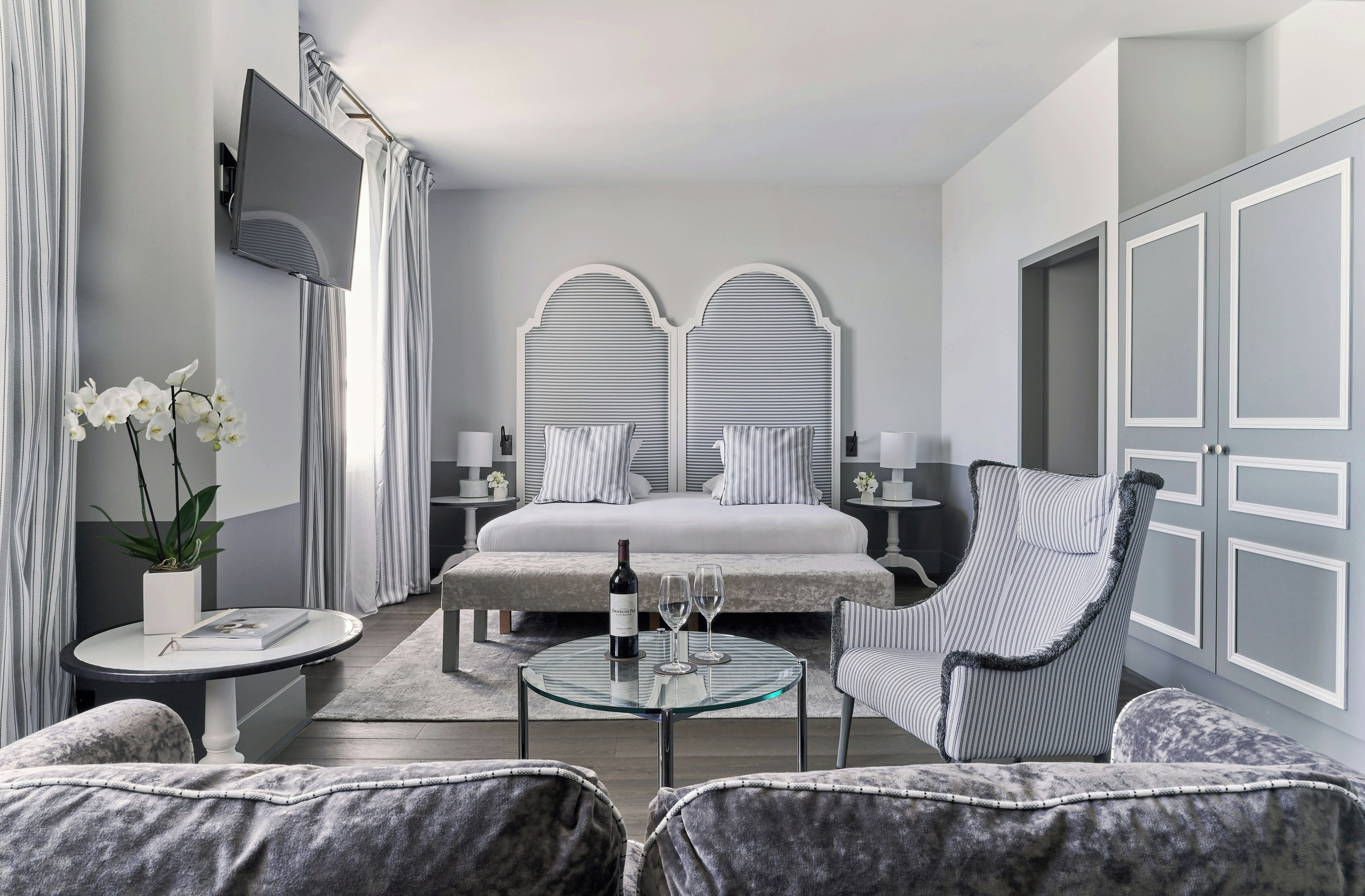 A modern hotel room with a bed, a seating area with a glass table, and a large window.