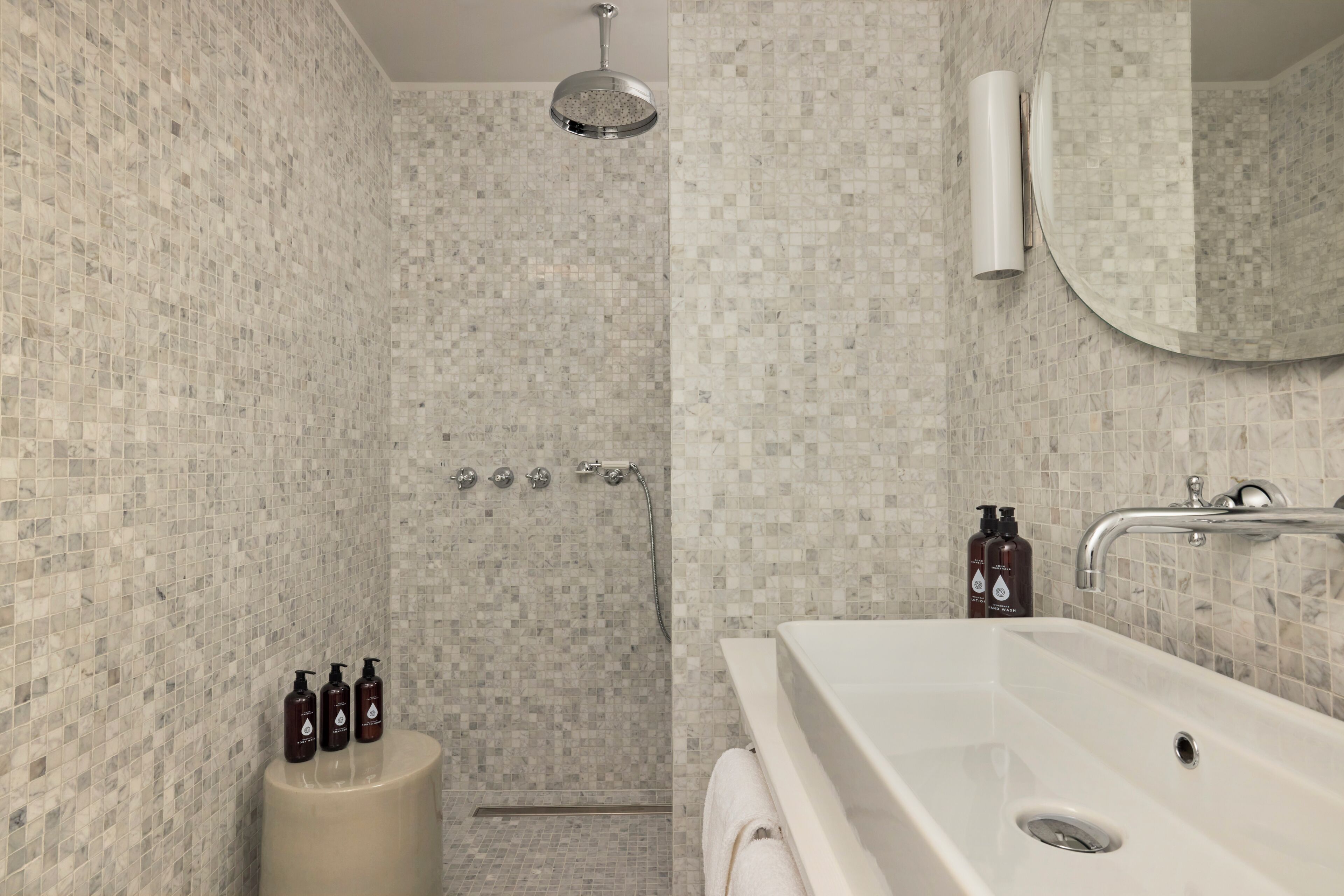 A bathroom with mosaic tile walls, a shower, a sink, and toiletries.