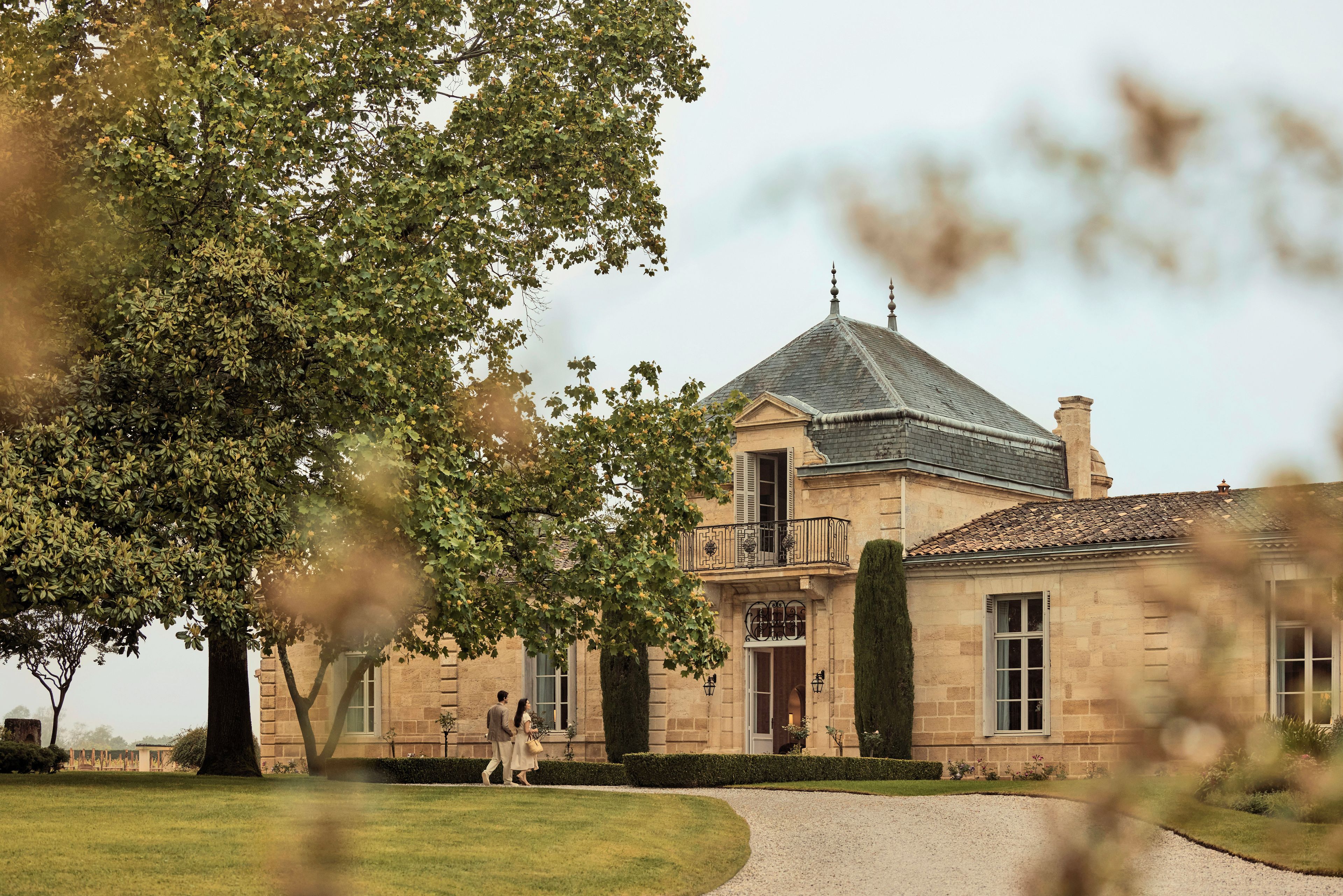 Un edificio de piedra histórico con un balcón destacado y un camino de grava que conduce a la entrada.