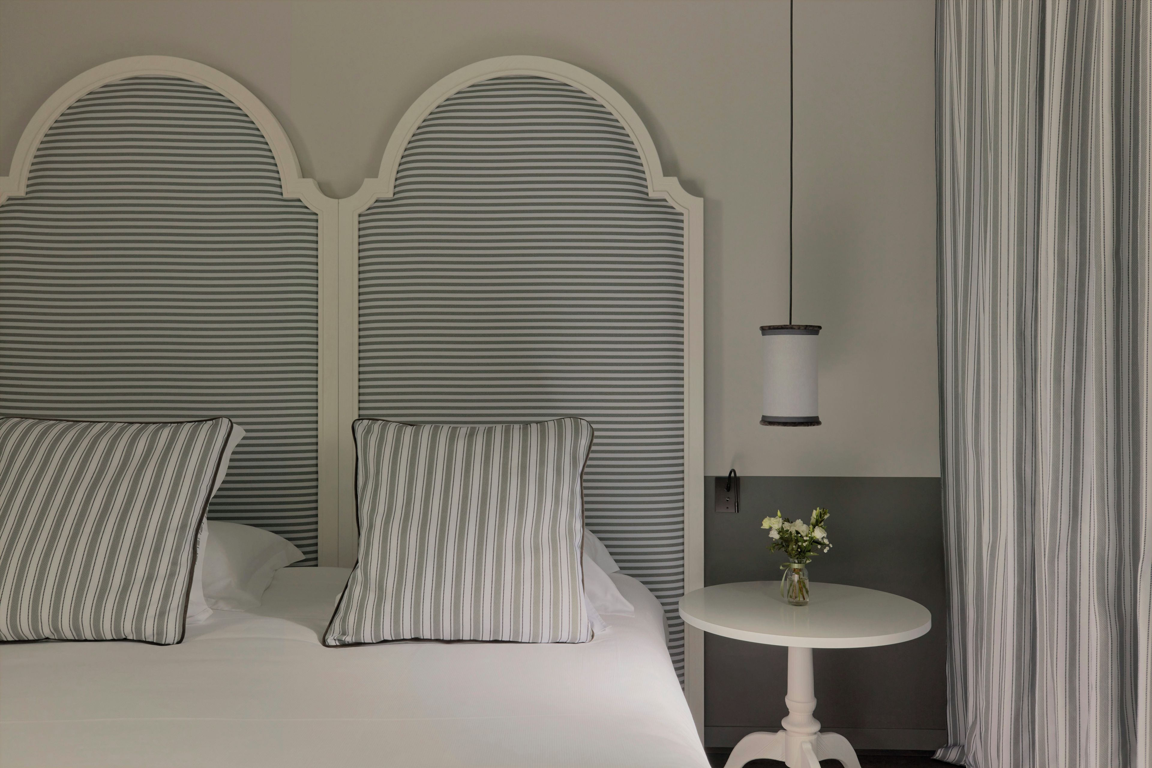 Habitación de hotel con una cama grande, dos almohadas, una mesita redonda con un florero y una lámpara.