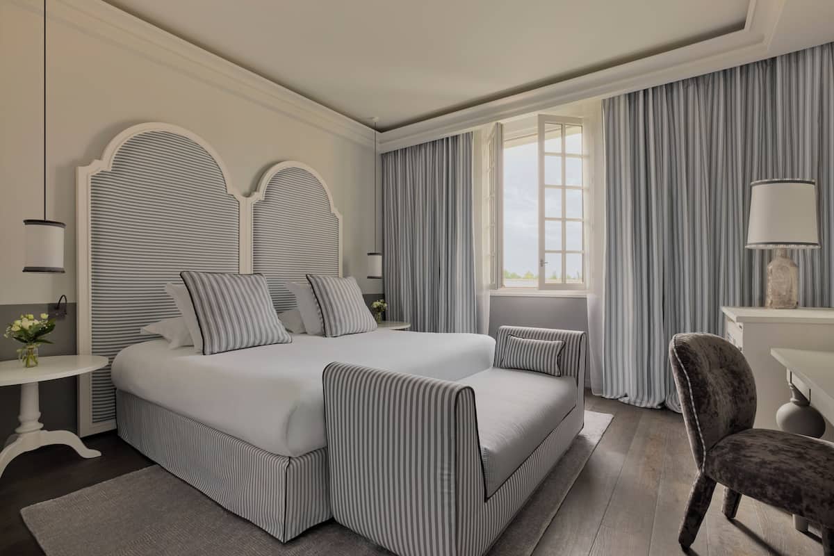 A modern bedroom with a large bed, a bedside table, a chair, and a window with curtains.