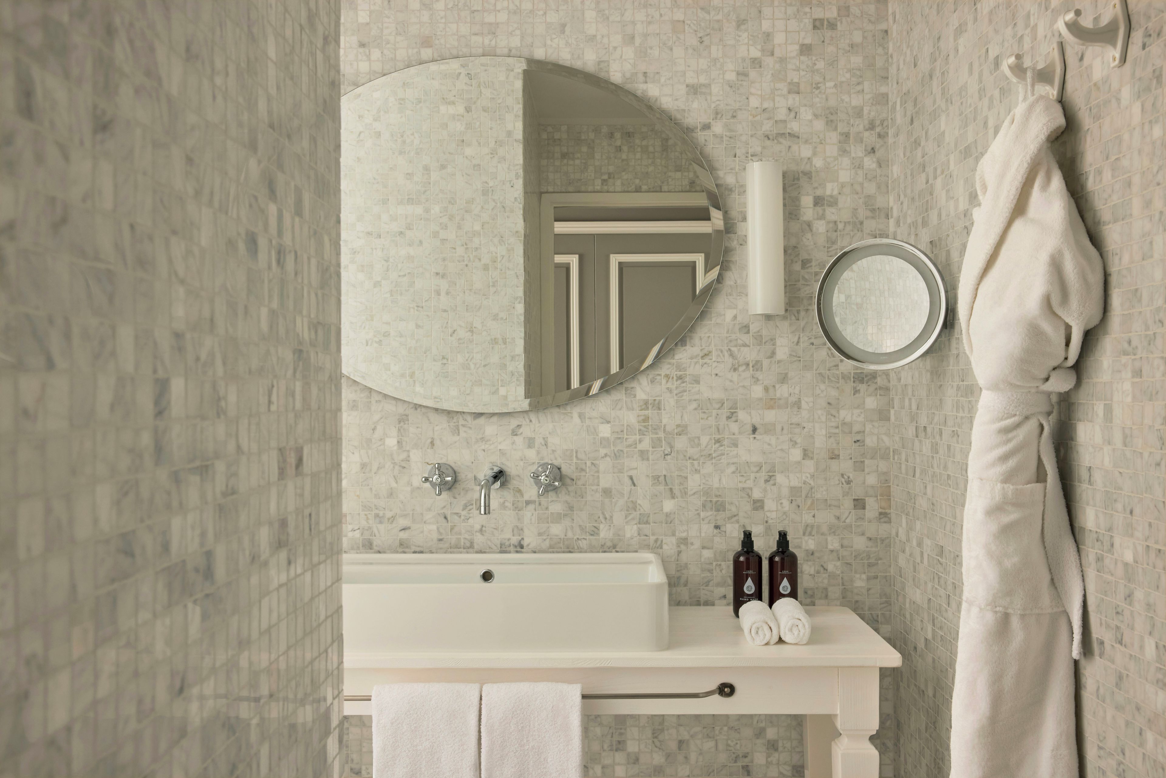 Une salle de bain avec un meuble-lavabo blanc, un miroir rond, un porte-serviettes et un rideau de douche.