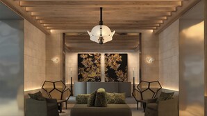 Un interior moderno con un sofá central, dos sillones, un muro con diseño geométrico y una lámpara colgante.