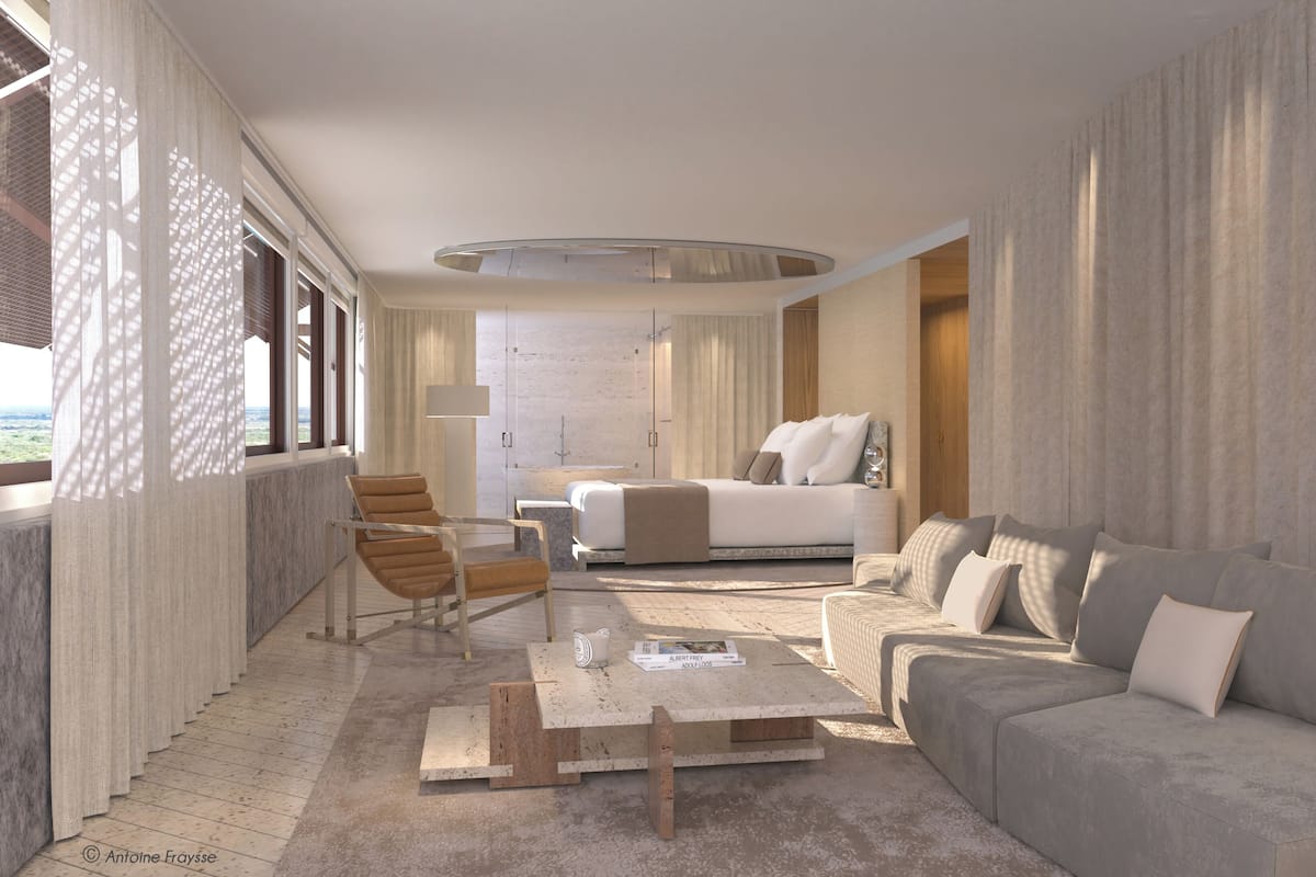 A modern hotel room with a large bed, a sofa, a coffee table, and a chair. There is a view of the outdoors through the windows.