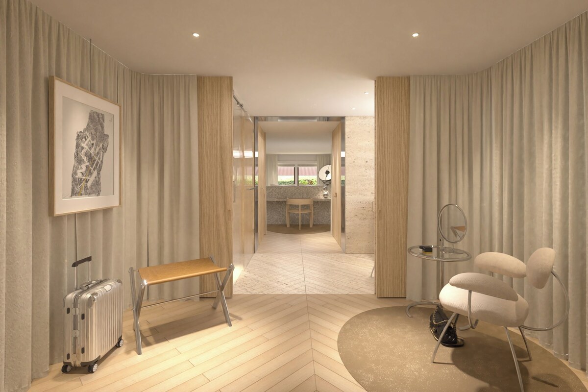 A modern hotel room with a wooden bench, a small table with a mirror, and a suitcase.