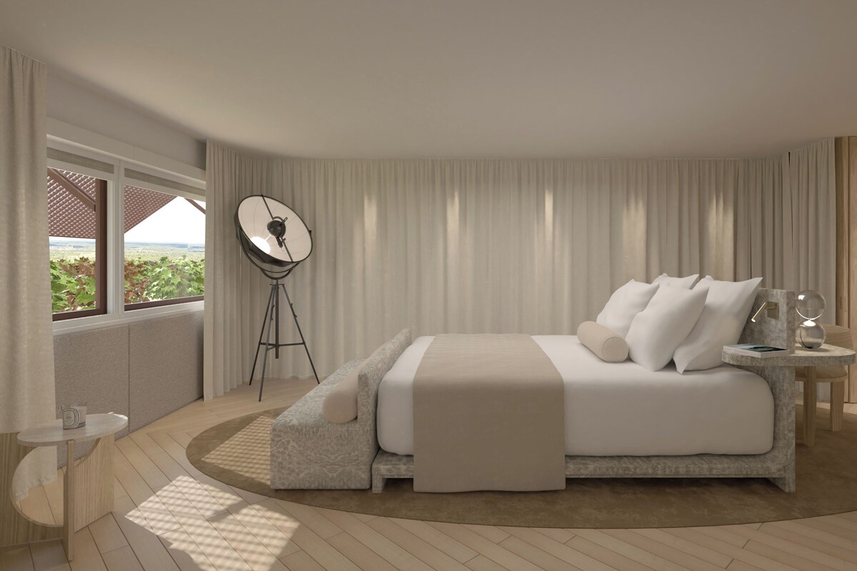 A modern bedroom with a large bed, a side table, a floor lamp, and a window with curtains.