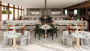 Un restaurante moderno con mesas redondas, asientos acolchados, ventanas amplias y un techo alto.