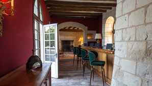 A bar area with a stone fireplace, green bar stools, and a wooden counter. - Château de Marçay (Marcay)