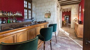 A bar area with wooden bar counter, green upholstered chairs, and a stone wall with a window. - Château de Marçay (Marcay)