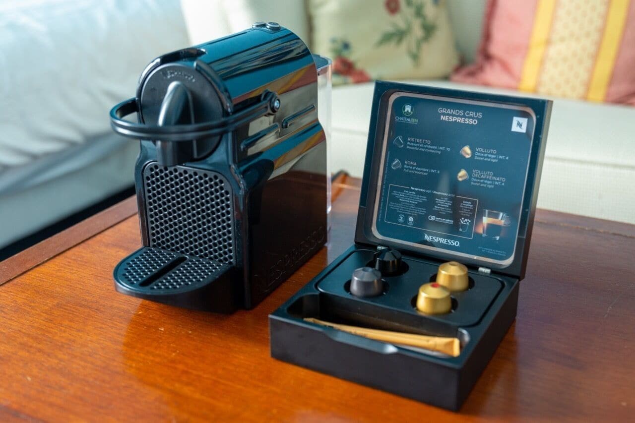 Una máquina de café Nespresso con su manual de instrucciones y sus accesorios sobre una mesa de madera.