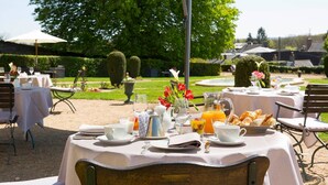An outdoor dining area with tables set for breakfast, surrounded by greenery and a well-maintained garden.