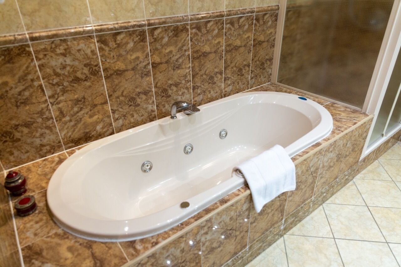 A bathroom with a large oval bathtub, marble tiles, and a shower area.
