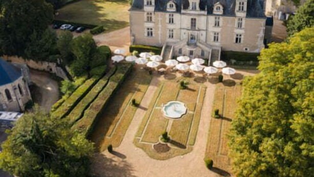 A large, historic building with a symmetrical garden and multiple outdoor seating areas.