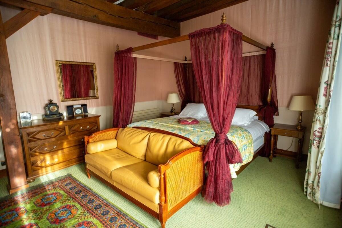 Un dormitorio con una cama con dosel, un aparador de madera, un sofá y una alfombra estampada.