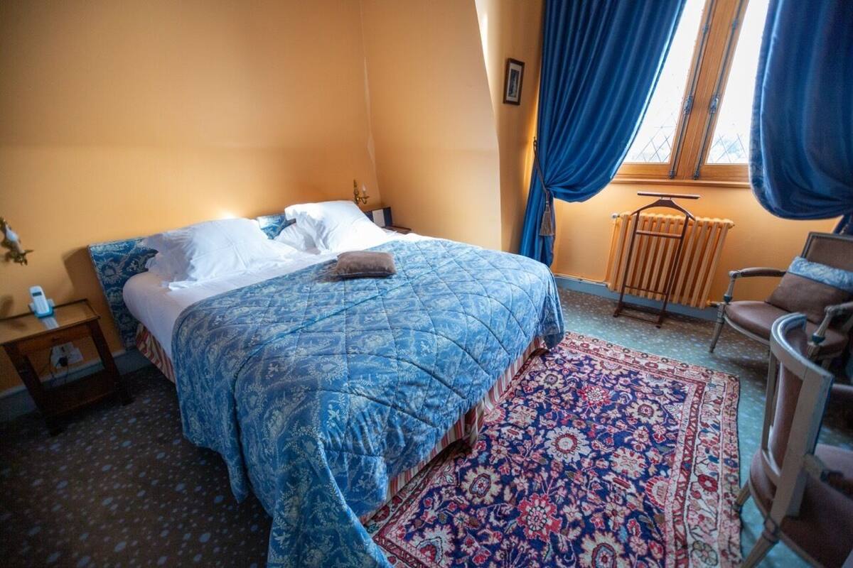 Un dormitorio con una cama grande, un tapete estampado, un radiador y una silla.