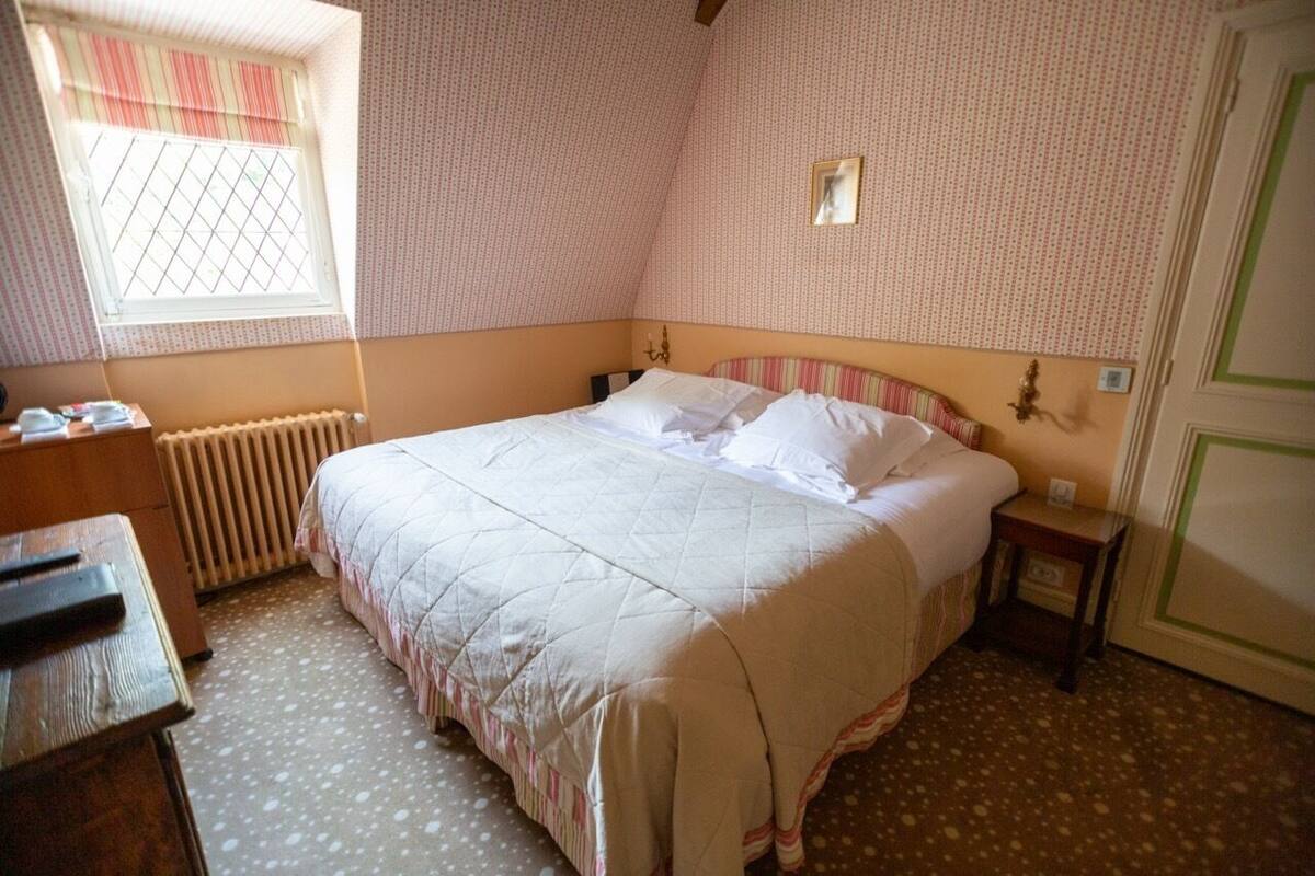 Un dormitorio con cama, mesita de noche, cómoda, ventana con cortinas y radiador.