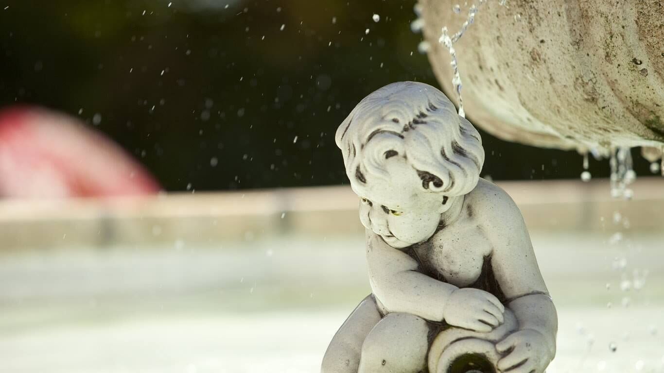Una statua in pietra raffigura un bambino seduto vicino a una fontana.