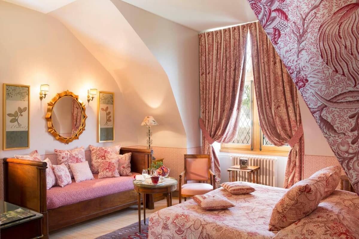 Un dormitorio acogedor con techo curvo, una cama grande con ropa de cama floral, un sofá, una silla y una pequeña mesa.