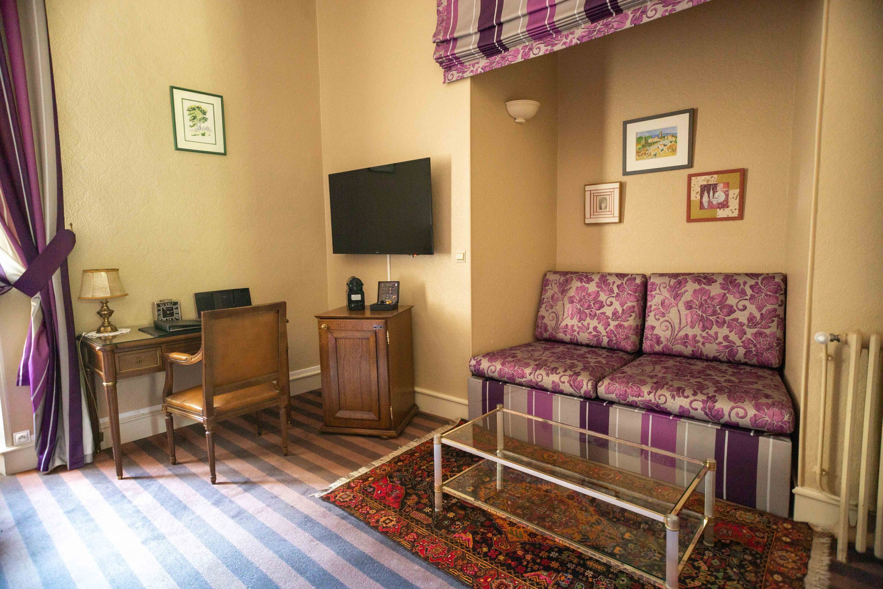 A living room with a sofa, a chair, a TV, a small cabinet, and a glass coffee table.