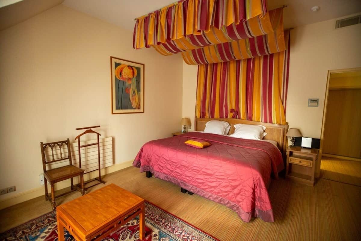 Un dormitorio con una cama grande, una silla de madera, una mesita pequeña y un tapete estampado.