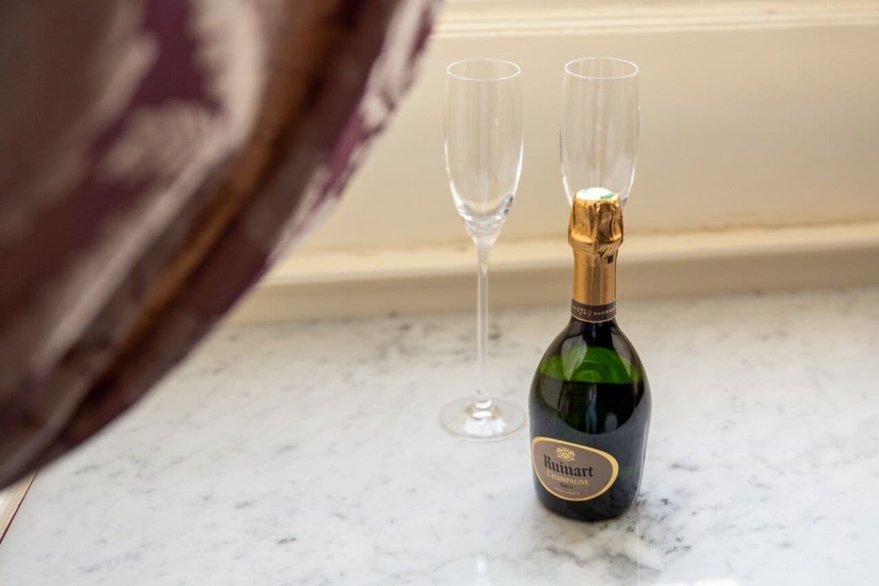 A bottle of Ruinart champagne and two empty glasses on a marble countertop.