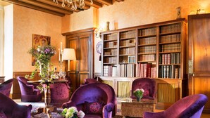 A library with bookshelves, a chandelier, and purple armchairs.