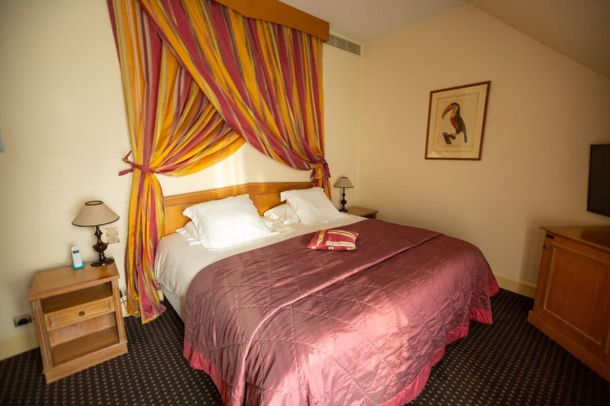 Una habitación de hotel con una cama, una mesita de noche, una lámpara, un televisor y un cuadro en la pared.