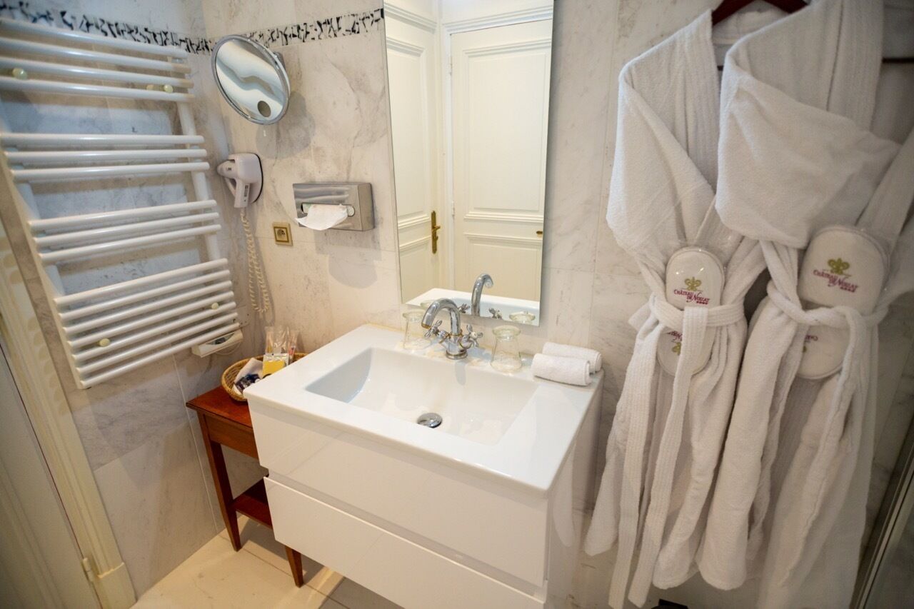Une salle de bain avec un lavabo blanc, un miroir, un porte-serviettes avec des peignoirs et un distributeur de serviettes.