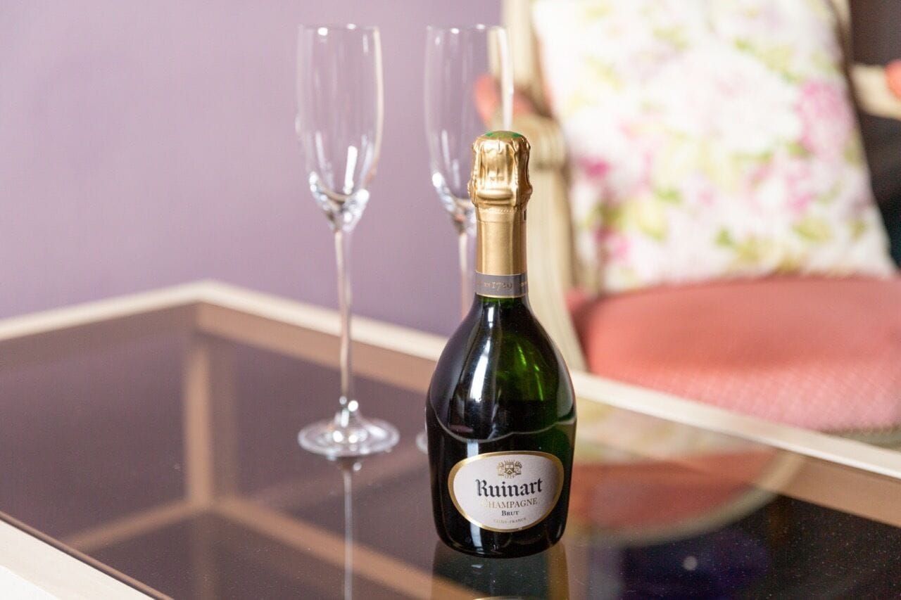 A Ruinart champagne bottle on a glass table with two empty champagne glasses.