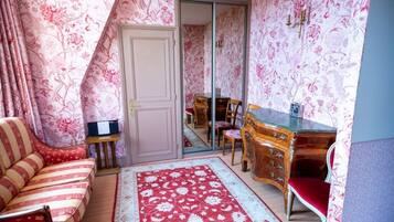 Une pièce avec une porte de placard miroir, un canapé à rayures, un bureau en bois et un tapis rouge à motifs.