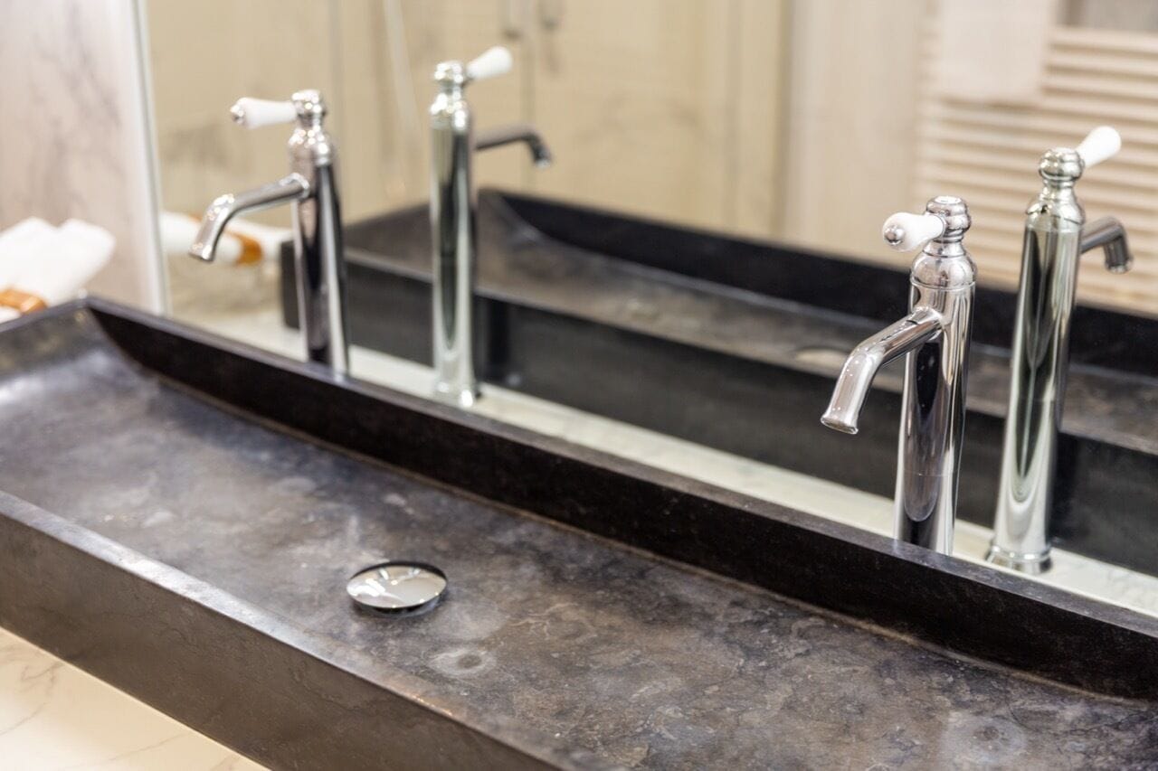 A bathroom with a black countertop, three chrome faucets, and a mirror reflecting the sink area.