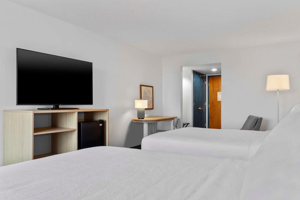 Een hotelkamer met twee bedden, een televisie, een bureau met lamp en een deur naar een andere kamer.